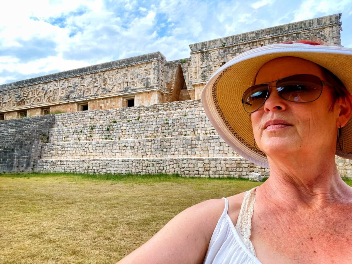 Amy, wearing a straw hat and sunglasses, looking out over the ancient stone structures of the Uxmal Mayan ruins in the Yucatan.