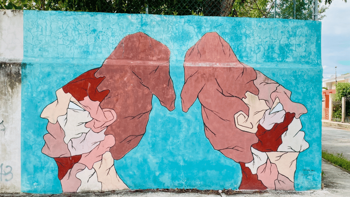 Colorful street mural of two Mayan faces on a turquoise wall in Mérida, Mexico