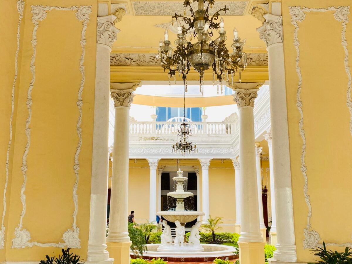 Ornate colonial mansion courtyard in Mérida Mexico with Corinthian columns, crystal chandelier, and tiered marble fountain