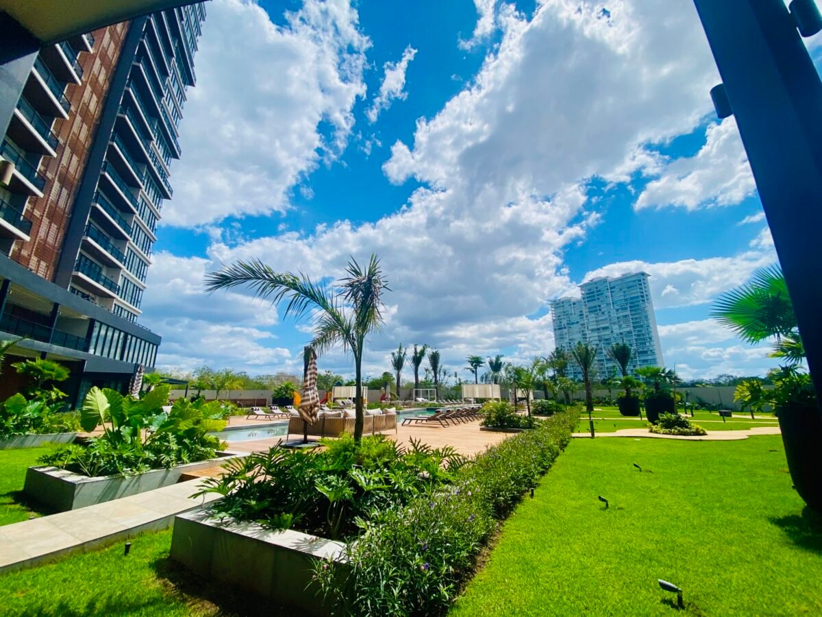 Art house highrise condo in North Merida with grass, vegetation, and pool with more highrises in the background