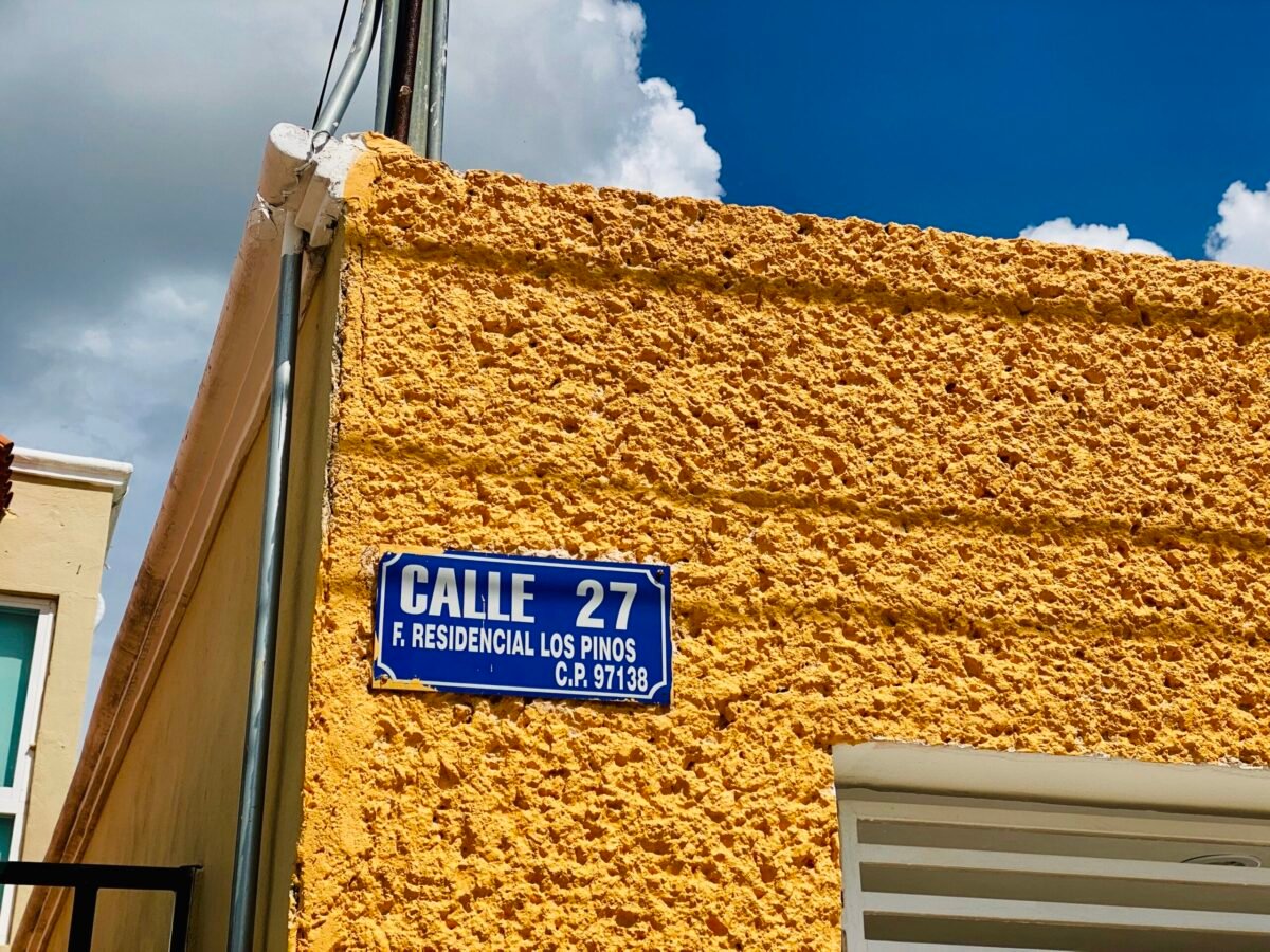 Blue street sign on a yellow house on a corner in a neighborhood in Merida Mexico