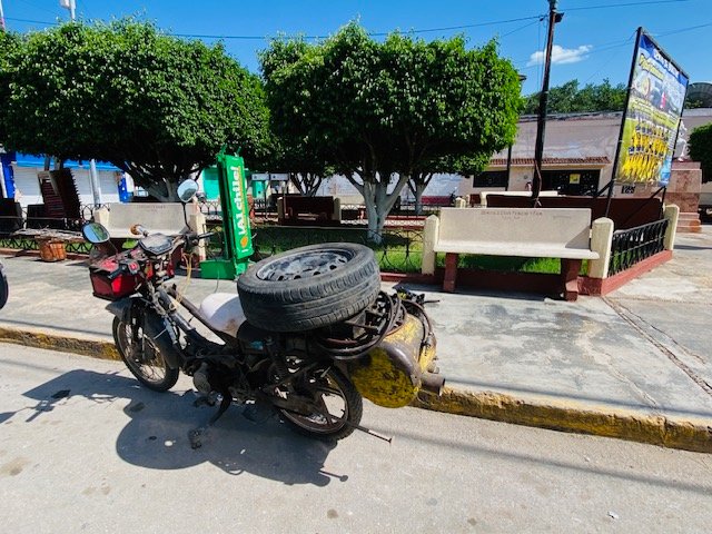 A motorcycle loaded with a car tire parked in a small town square in Yucatán, Mexico — everyday local life outside of Mérida